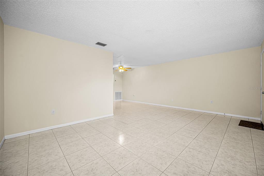An empty room features light-colored tile flooring, beige walls, and a ceiling fan — 5750 80TH STREET N UNIT D101, ST PETERSBURG, FL