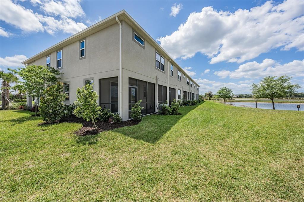 A multi-story townhouse exterior features a screened-in patio and a grassy yard near a pond — 19219 BLUE POND DRIVE, LUTZ, FL