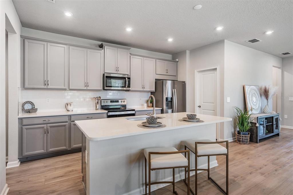 A kitchen features gray cabinets, white countertops, a central island, and stainless steel appliances — 19219 BLUE POND DRIVE, LUTZ, FL