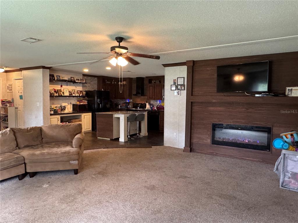 A living room with carpet, a brown sectional sofa, and a fireplace with a mounted television — 1916 FRUITLAND PARK BOULEVARD, FRUITLAND PARK, FL