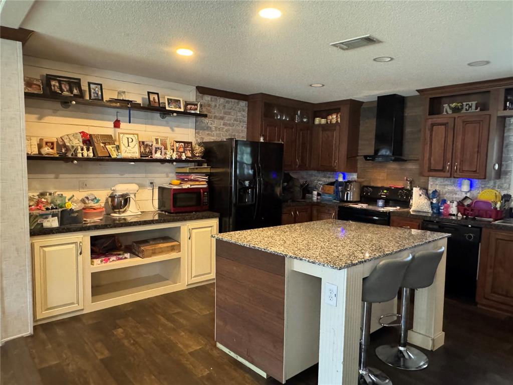 A kitchen features dark wood cabinets, a granite-topped island, open shelving, and a black refrigerator — 1916 FRUITLAND PARK BOULEVARD, FRUITLAND PARK, FL