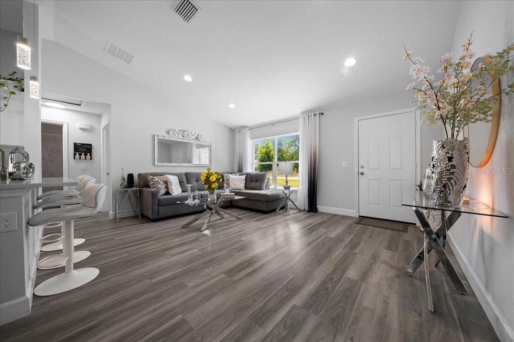 A living room features gray wood-look flooring, a sectional sofa, and a white front door — 13789 SW 102ND PLACE, DUNNELLON, FL