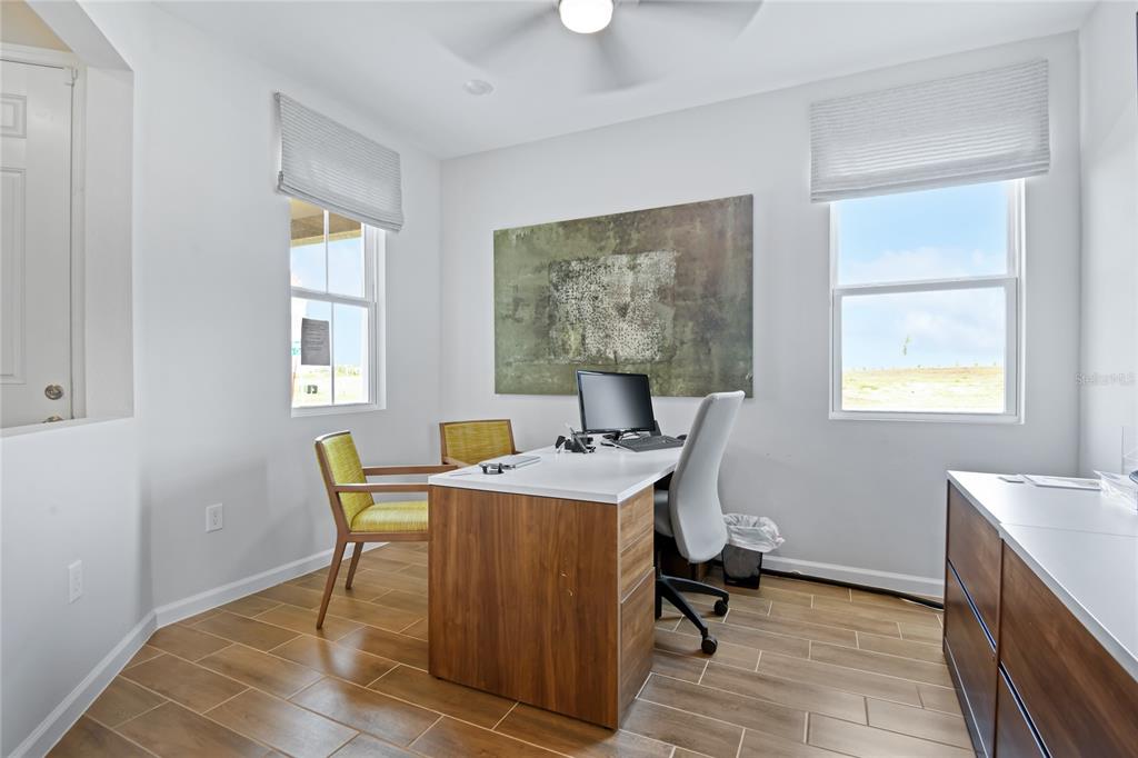 A home office features a desk, two chairs, wood-look tile flooring, and two windows — 2521 29TH LANE E, PALMETTO, FL