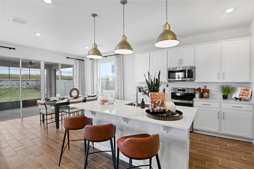 A modern kitchen features white cabinets, a quartz island with bar stools, and dining area — 2521 29TH LANE E, PALMETTO, FL