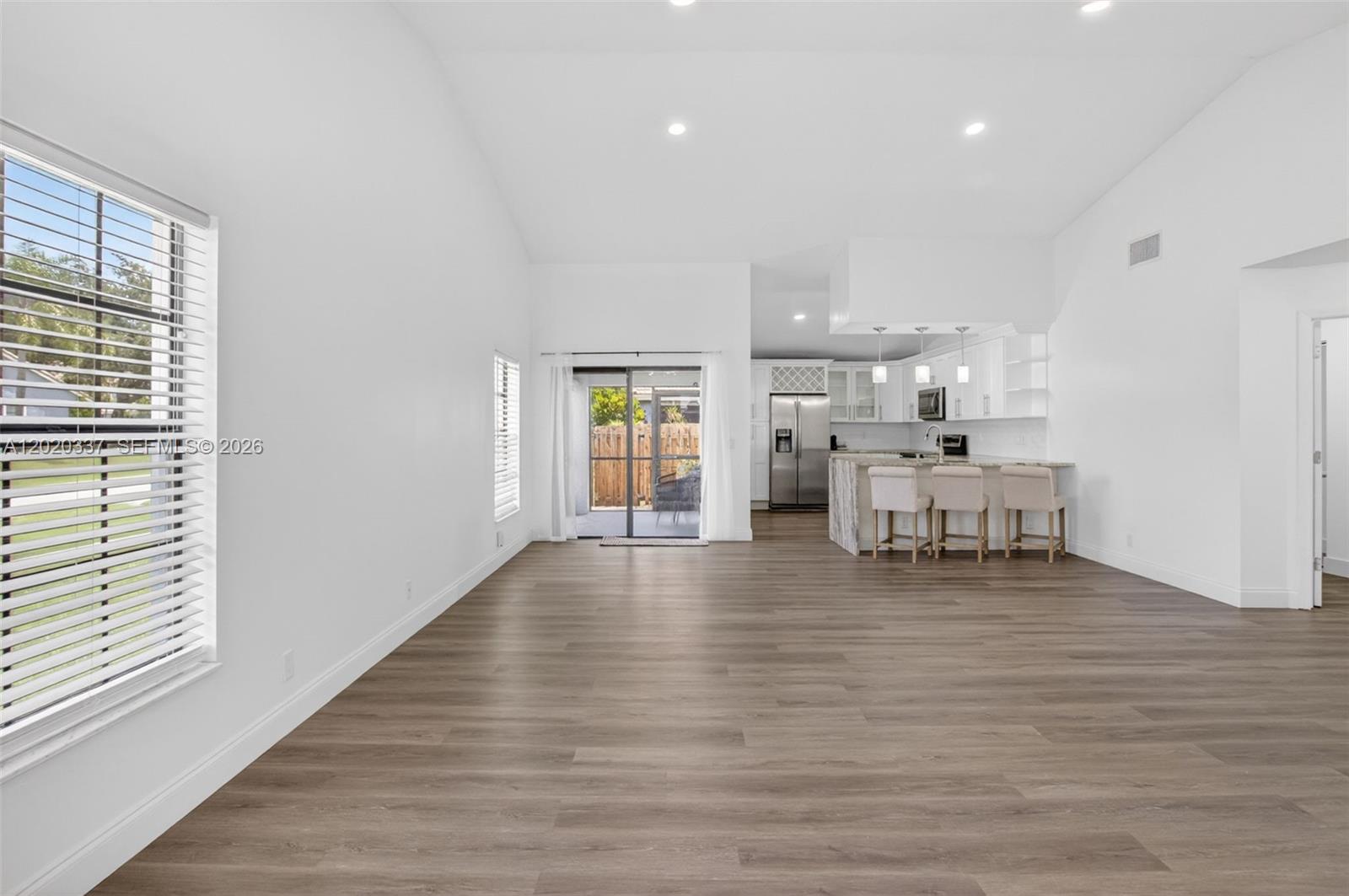 An open-concept living area features wood-look flooring, white walls, and a kitchen with bar seating — 9912 S 61st Way S # A, Boynton Beach FL 33437, BOYNTON BEACH, FL