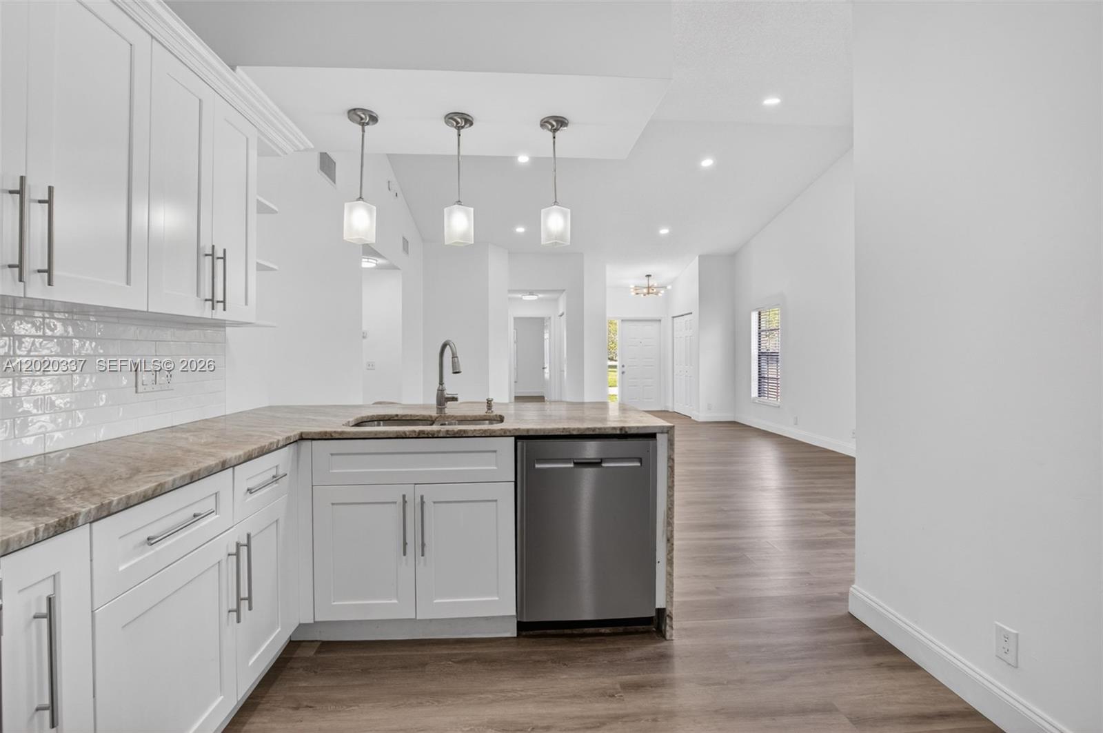 A modern kitchen with white cabinets, stone countertops, and stainless steel appliances overlooks a living area — 9912 S 61st Way S # A, Boynton Beach FL 33437, BOYNTON BEACH, FL