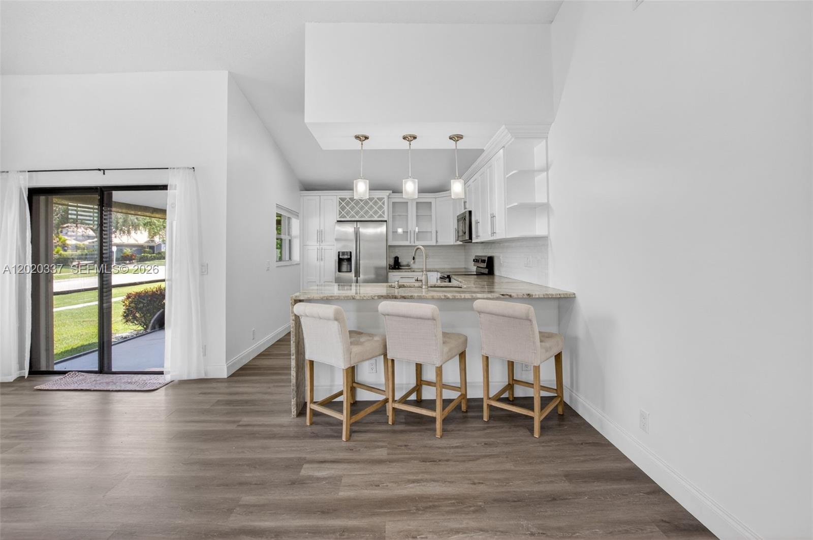 A kitchen features white cabinets, a stone countertop, three bar stools, and sliding glass doors — 9912 S 61st Way S # A, Boynton Beach FL 33437, BOYNTON BEACH, FL