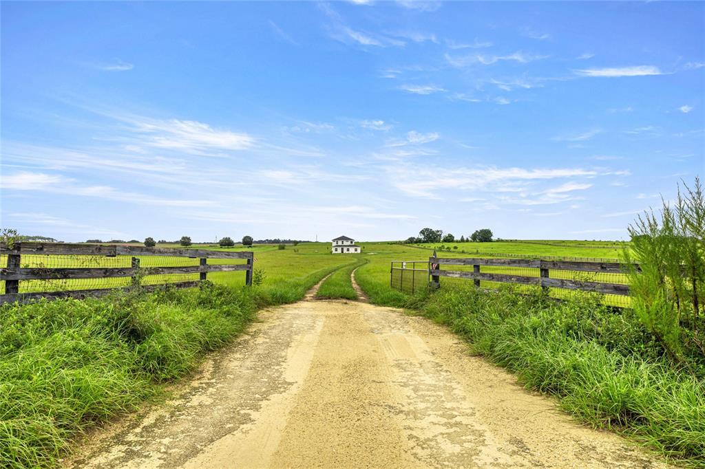 A dirt driveway leads through a wooden fence toward a distant house in a grassy field — 21786 NW 27TH STREET, MORRISTON, FL