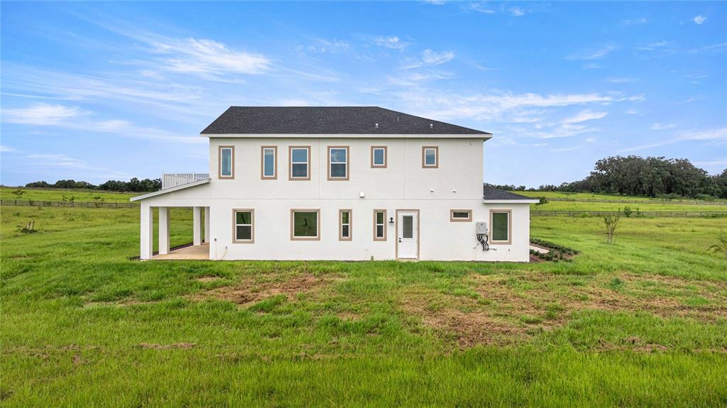 The exterior of a two-story white house with a covered patio sits in a field — 21786 NW 27TH STREET, MORRISTON, FL