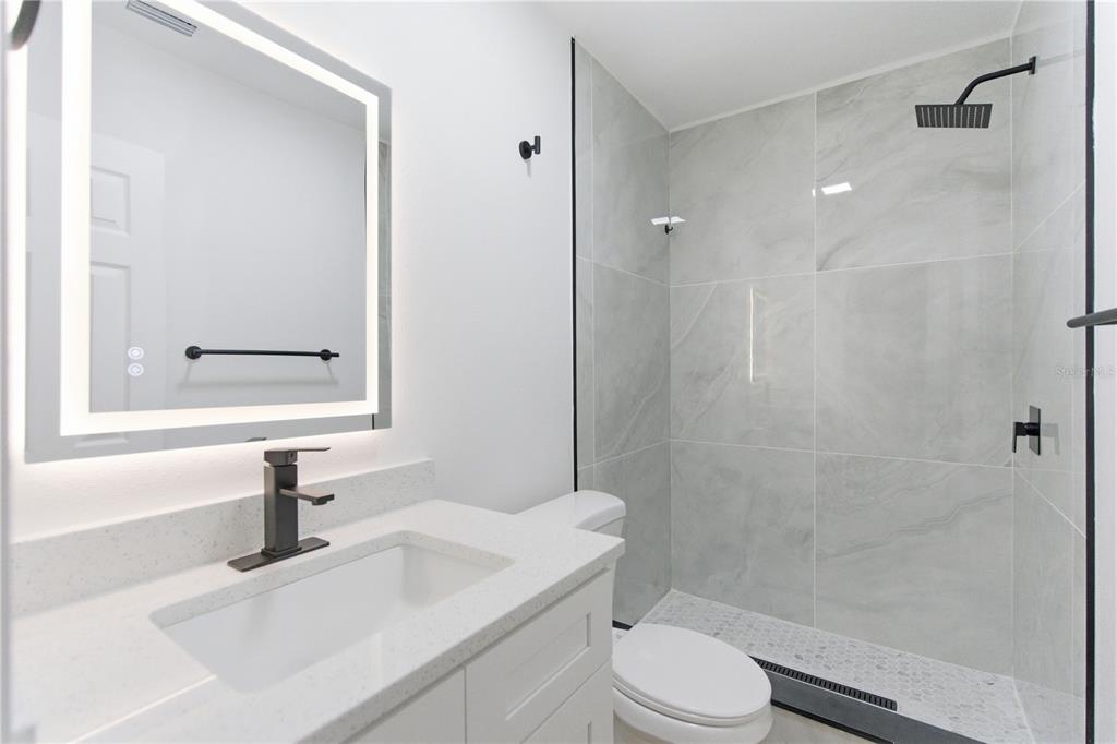 A modern bathroom features a white vanity, a lighted mirror, and a tiled walk-in shower — 10945 N BOULEVARD, TAMPA, FL