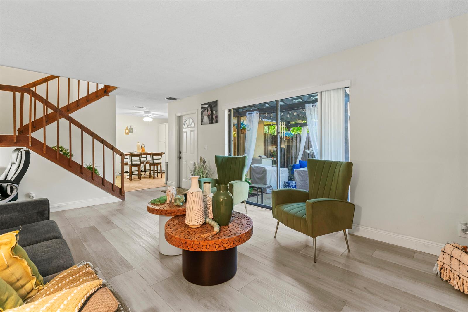 A living room features wood-look flooring, a wooden staircase, green armchairs, and a sliding glass door — 1630 Forest Lakes Circle # C, West Palm Beach FL 33406, WEST PALM BEACH, FL