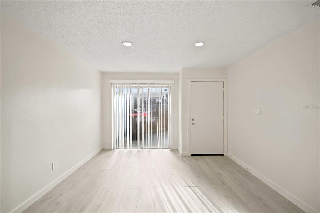 A bright, empty room features light-colored wood-look flooring, white walls, and a sliding glass door — 5395 SE 30TH PLACE ALL UNITS, OCALA, FL