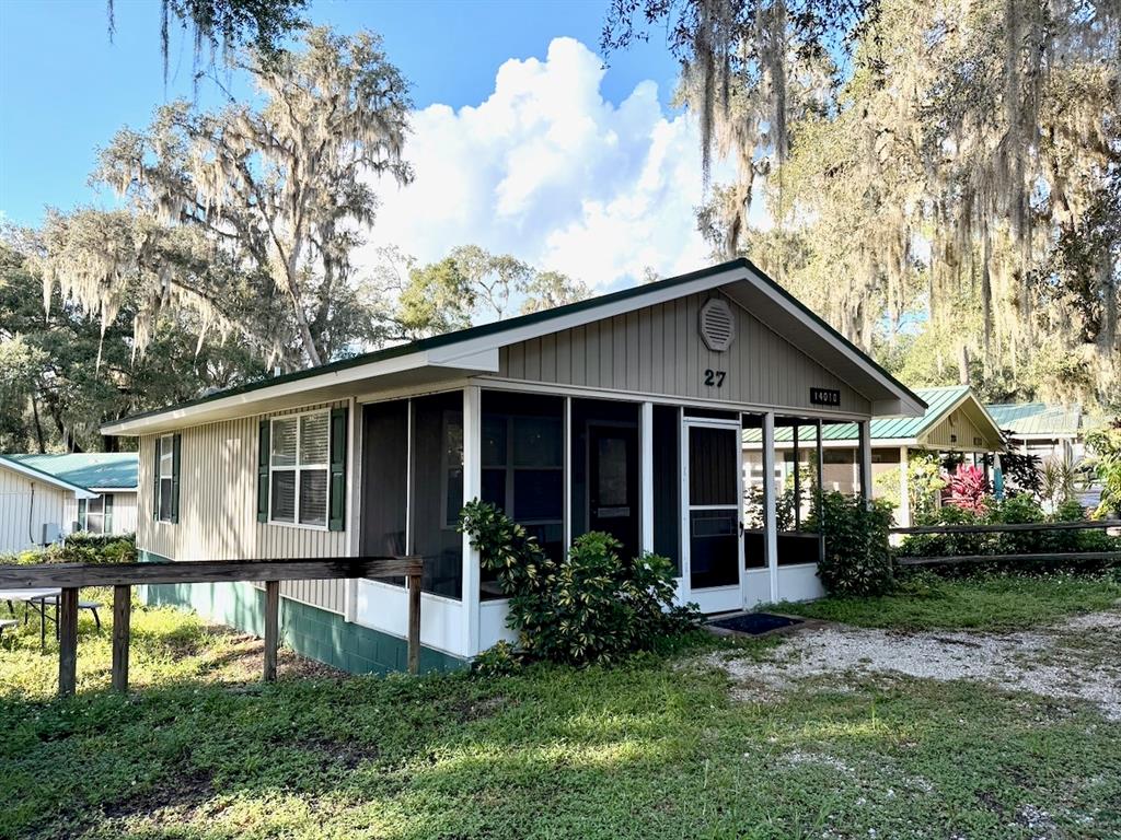 A single-story house with tan vertical siding, a screened-in front porch, and green trim — 14010 NE 250TH CIRCLE, SALT SPRINGS, FL