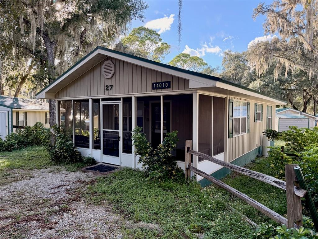 A tan mobile home features a screened-in front porch and a gravel driveway — 14010 NE 250TH CIRCLE, SALT SPRINGS, FL