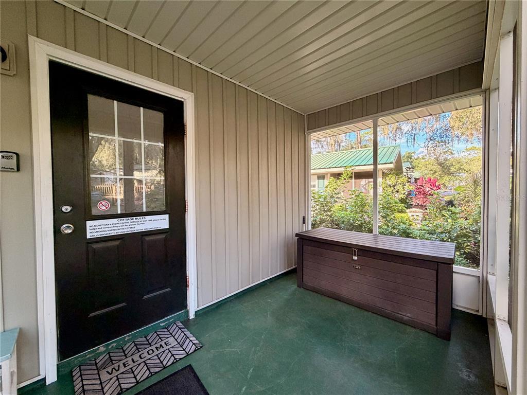A screened-in porch features a black front door, green flooring, and a brown storage chest — 14010 NE 250TH CIRCLE, SALT SPRINGS, FL