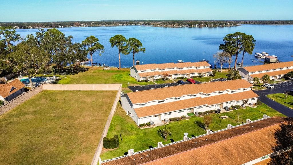 An aerial view shows multi-unit townhomes with brown roofs situated near a large lake — 11001 SE SUNSET HARBOR ROAD UNIT F45, SUMMERFIELD, FL