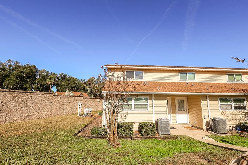 A two-story tan vinyl-sided townhouse with a white front door and two exterior air conditioners — 11001 SE SUNSET HARBOR ROAD UNIT F45, SUMMERFIELD, FL