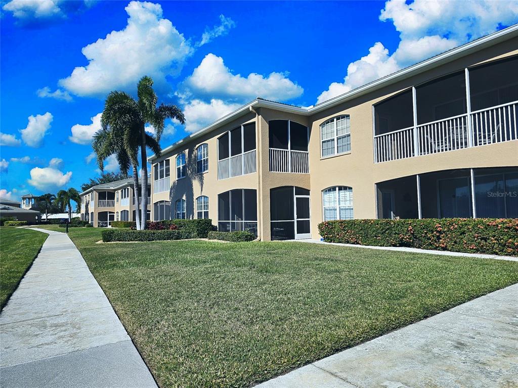 A multi-story apartment building with screened-in balconies and a sidewalk on a sunny day — 6446 7TH AVENUE CIRCLE W UNIT 6446, BRADENTON, FL