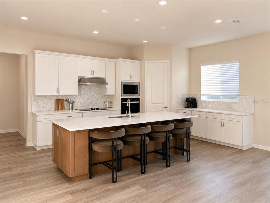 A kitchen features white cabinets, a wood-toned island with four stools, and light-colored flooring — 4330 SUNSET PRESERVE BLVD, ORLANDO, FL