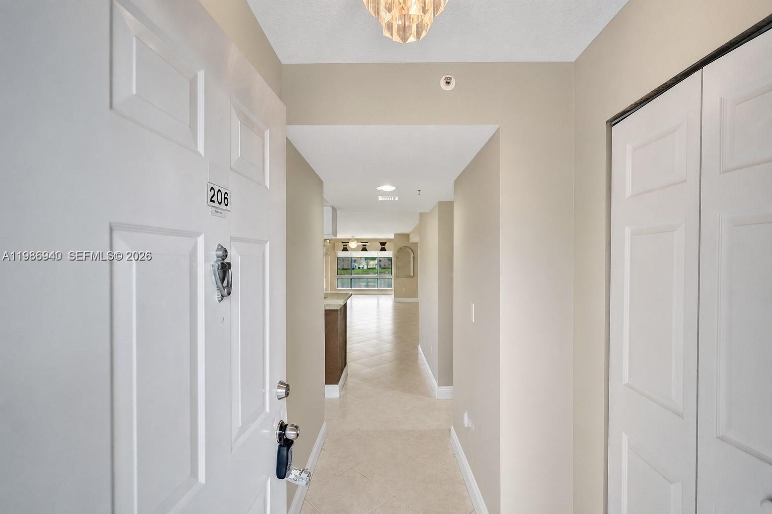 An outdoor apartment hallway features a beige stucco wall, a white screen door, and windows — 12547 Imperial Isle Dr # 206, Boynton Beach FL 33437, BOYNTON BEACH, FL