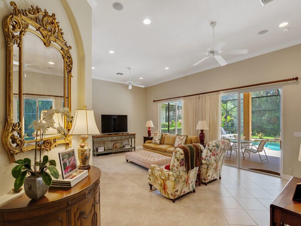 A living room with a large gold mirror, floral armchairs, and a view of a pool — 1225 Riverwind Circle, Vero Beach FL 32967, VERO BEACH, FL