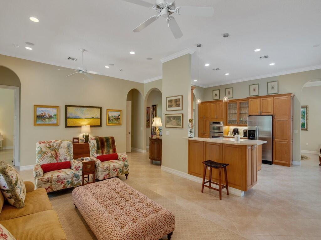 A living room with floral chairs and a kitchen with wooden cabinets and an island — 1225 Riverwind Circle, Vero Beach FL 32967, VERO BEACH, FL