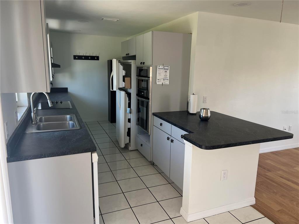 A kitchen with a breakfast bar and tile flooring opens to a wood-floored living area — 10934 FREEDOM BOULEVARD, SEMINOLE, FL