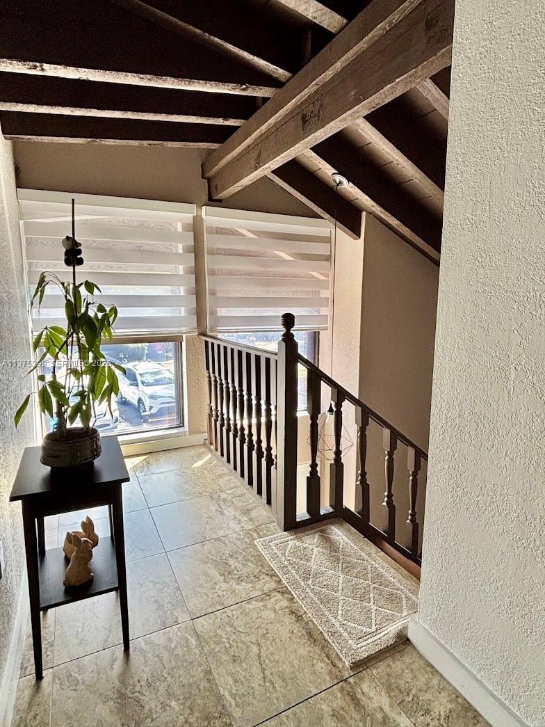 A landing with tile floors, a wooden staircase railing, and exposed ceiling beams — 6937 SW 115th Pl # C37, Miami FL 33173, MIAMI, FL
