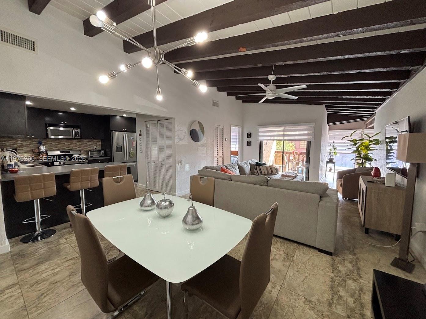 An open-concept living and dining area features dark wood ceiling beams and tile flooring — 6937 SW 115th Pl # C37, Miami FL 33173, MIAMI, FL