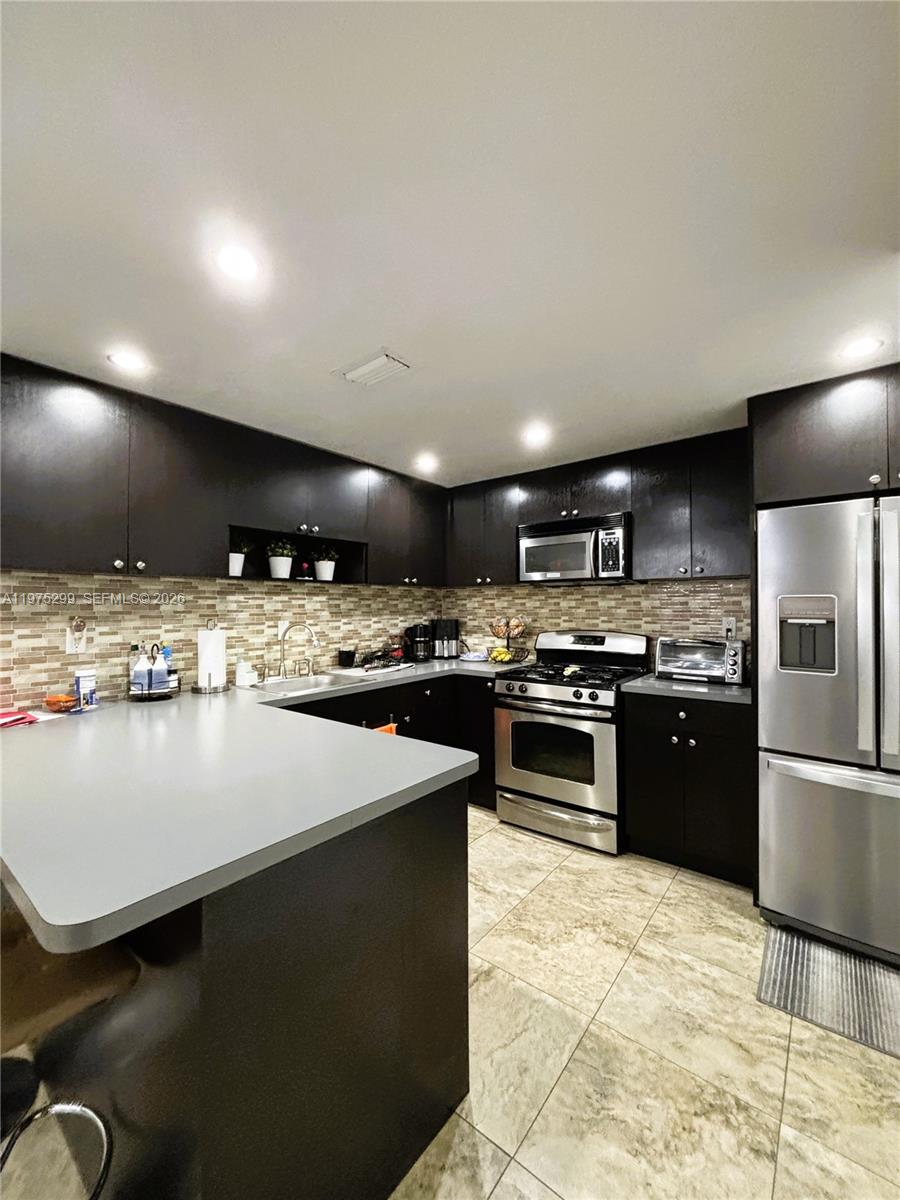 A kitchen features dark cabinetry, stainless steel appliances, a gray countertop, and a tiled backsplash — 6937 SW 115th Pl # C37, Miami FL 33173, MIAMI, FL