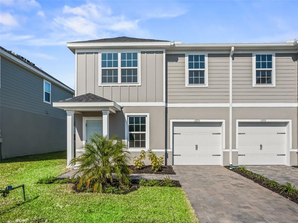 A two-story townhouse exterior features gray siding, a covered entryway, and two attached garages — 1205 PORT BLUE WAY, LADY LAKE, FL