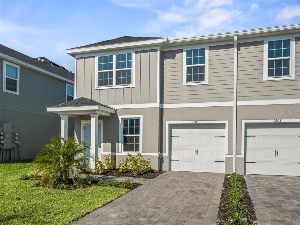 A two-story townhouse with a gray exterior, a single-car garage, and a paved driveway — 1205 PORT BLUE WAY, LADY LAKE, FL