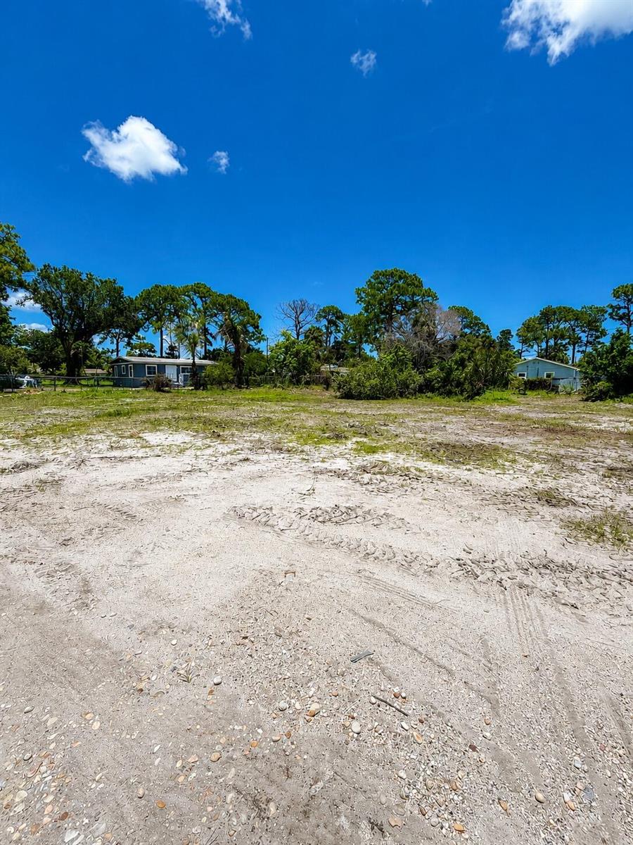 A wide, sandy vacant lot features sparse vegetation and distant houses under a blue sky — 444 53rd Drive N, FL 33415, FL