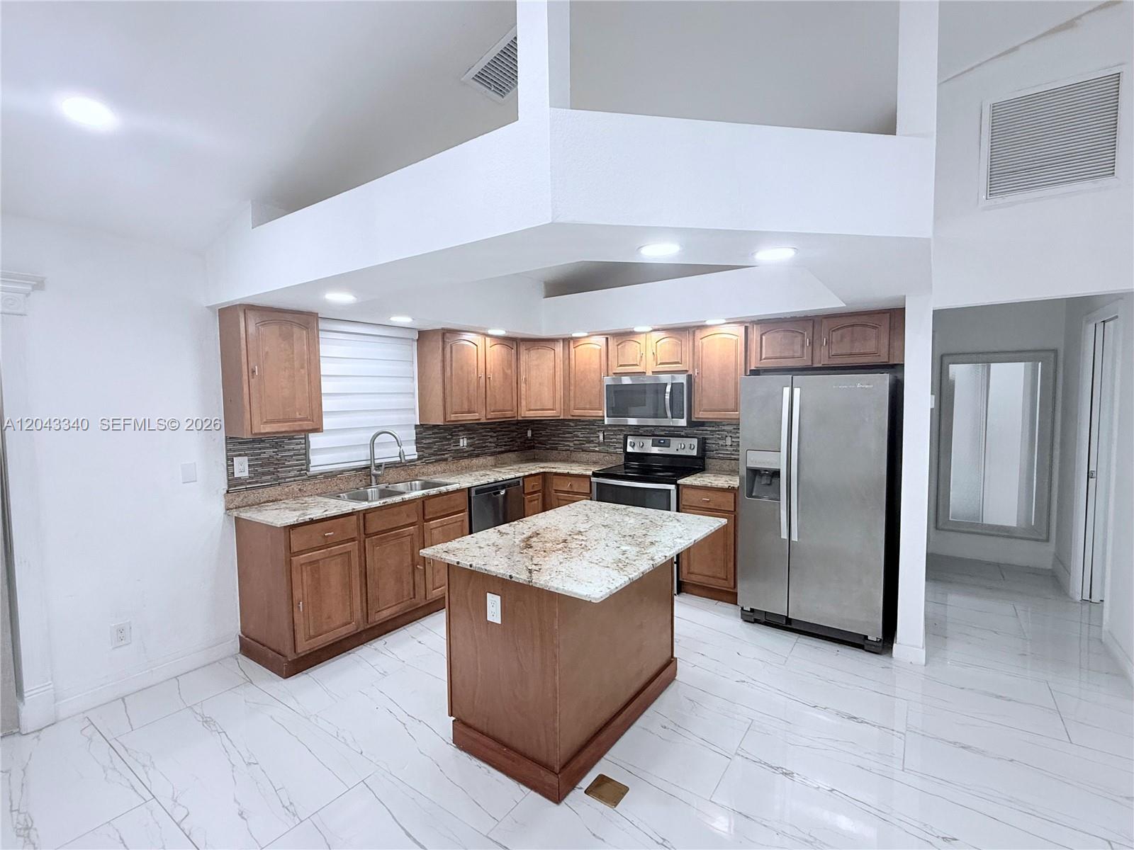 A kitchen features wood cabinets, granite countertops, stainless steel appliances, and white marble-look tile flooring — 313 NW 16 PL, Cape Coral FL 33993, CAPE CORAL, FL