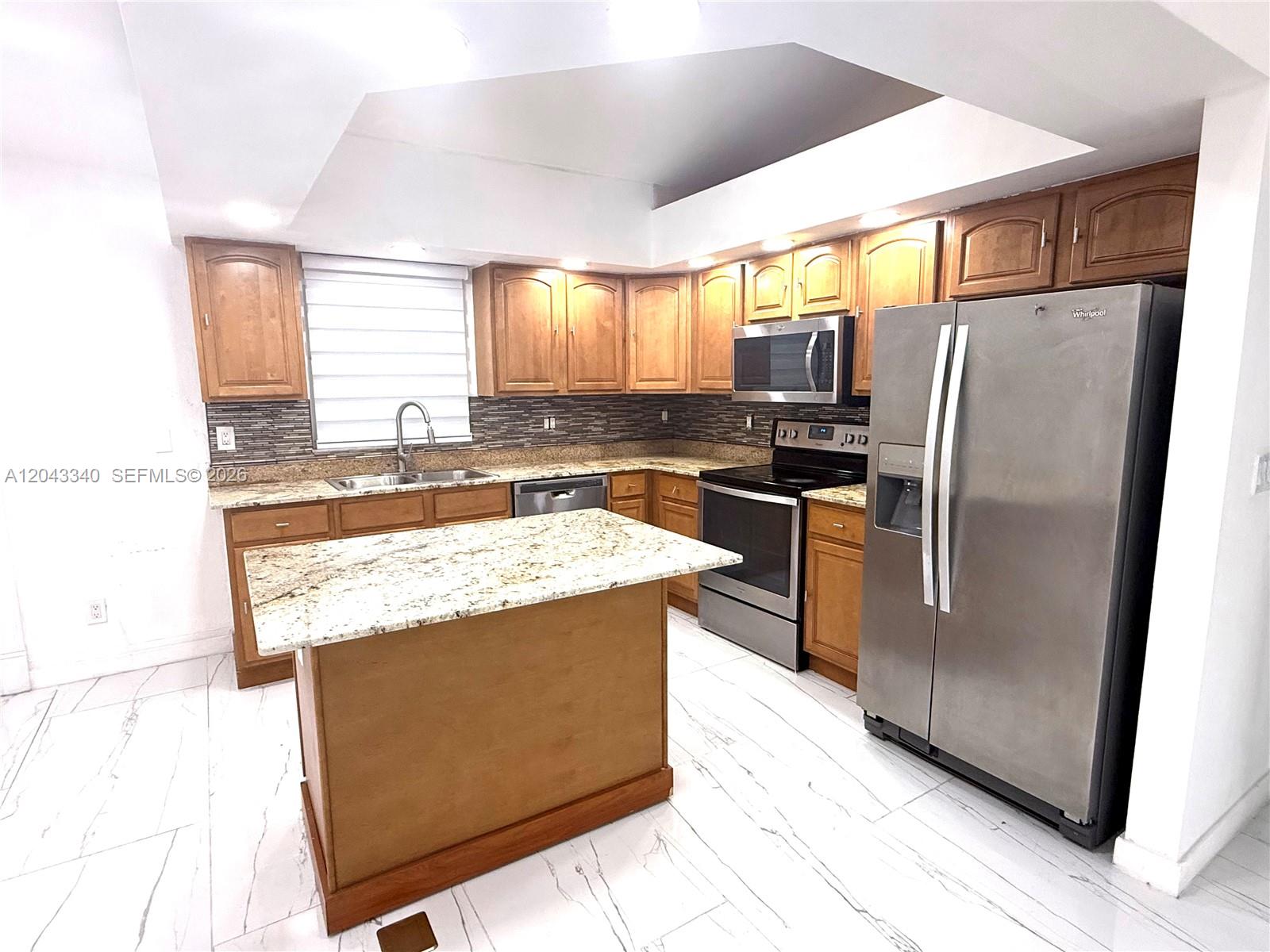A kitchen features wood cabinets, granite countertops, stainless steel appliances, and white marble-patterned tile flooring — 313 NW 16 PL, Cape Coral FL 33993, CAPE CORAL, FL