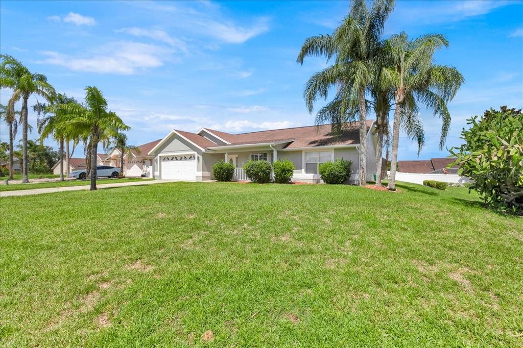 A single-story house with a white garage, a front porch, and palm trees in the yard — 112 AZALEA DRIVE, DAVENPORT, FL