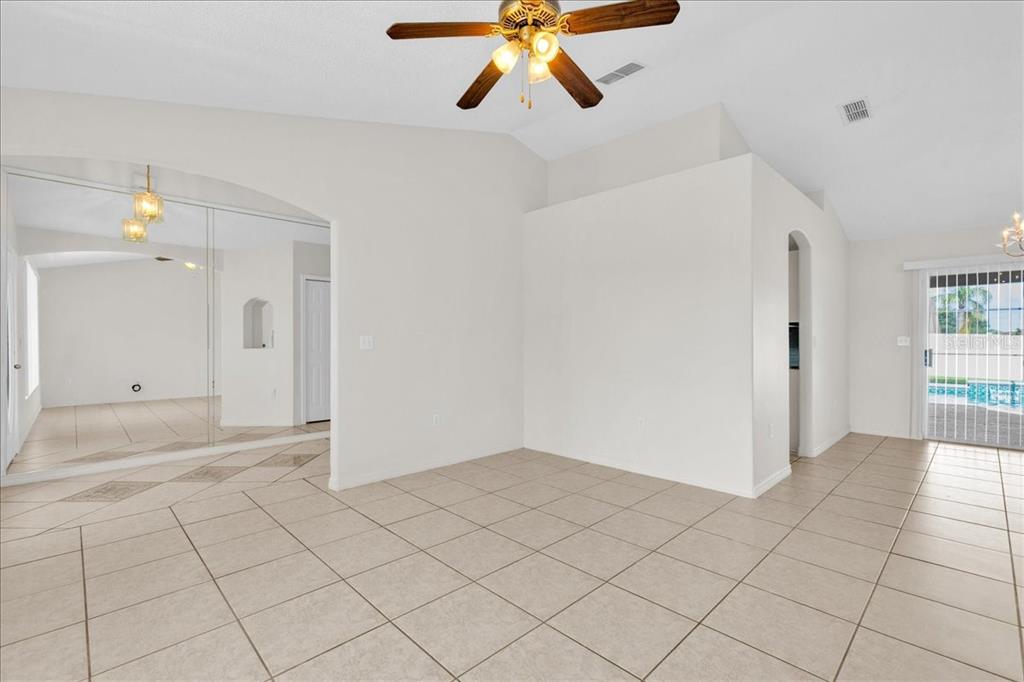A bright, tiled living area features a vaulted ceiling, a ceiling fan, and mirrored walls — 112 AZALEA DRIVE, DAVENPORT, FL