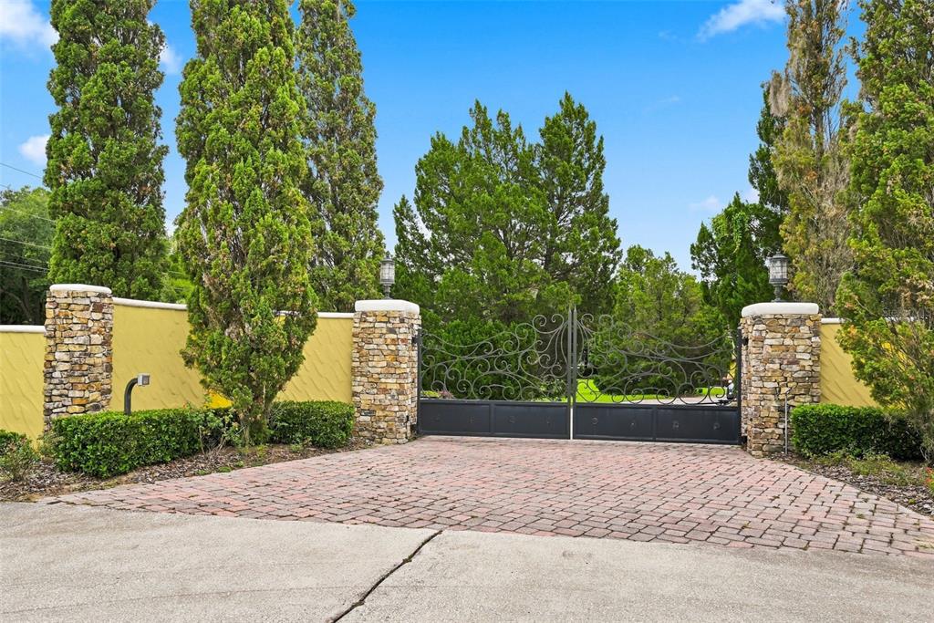 A brick driveway leads to a black metal gate flanked by stone pillars and walls — 9679 WESTOVER ROBERTS RD, WINDERMERE, FL