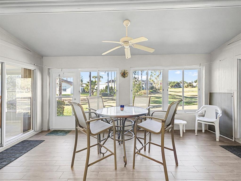 A sunroom features a dining set, light wood-look flooring, a ceiling fan, and large windows — 11625 BARONWOOD COURT, HUDSON, FL