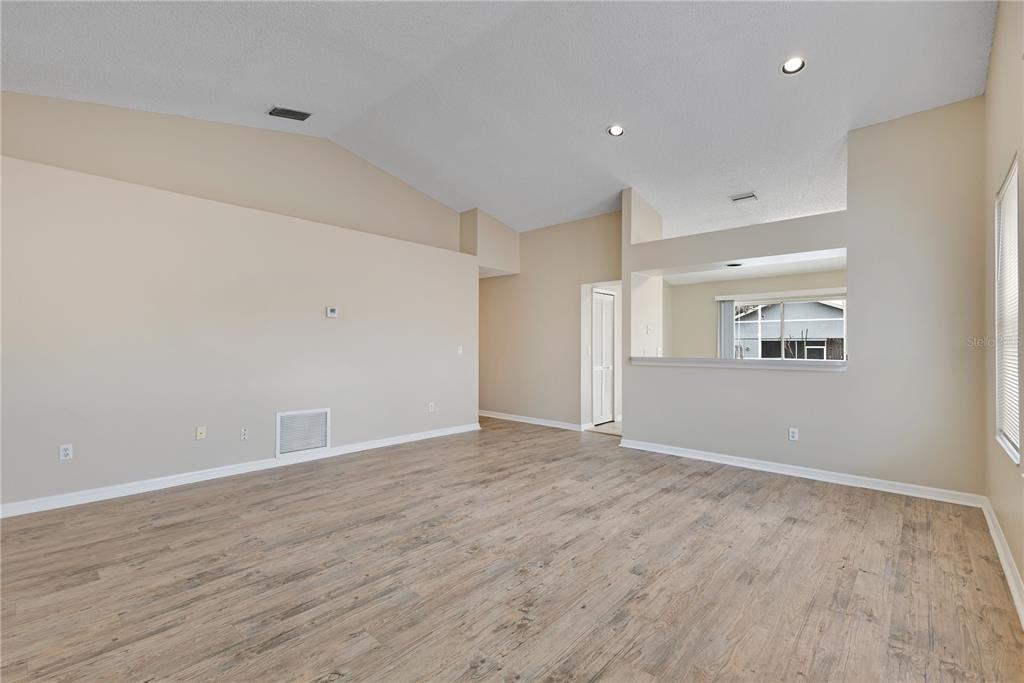 An empty living room features vaulted ceilings, light-colored walls, and wood-look flooring — 8821 PARLIAMENT COURT, KISSIMMEE, FL