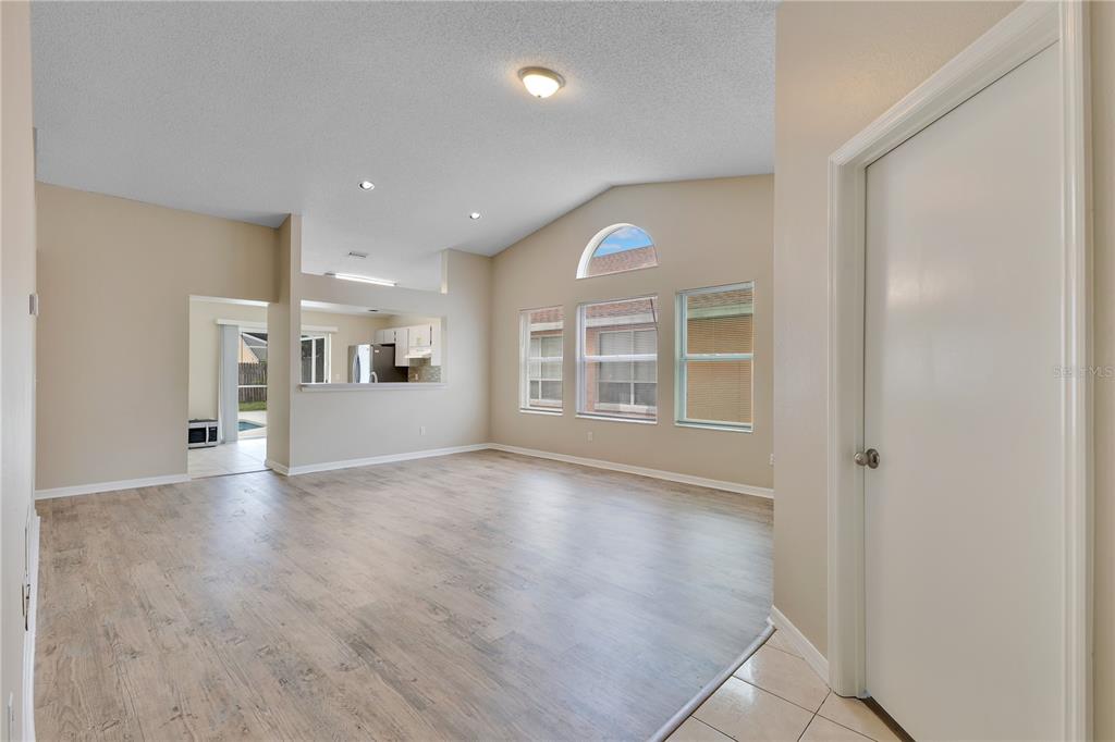 A living room with light wood-look flooring, vaulted ceilings, and a view into the kitchen — 8821 PARLIAMENT COURT, KISSIMMEE, FL