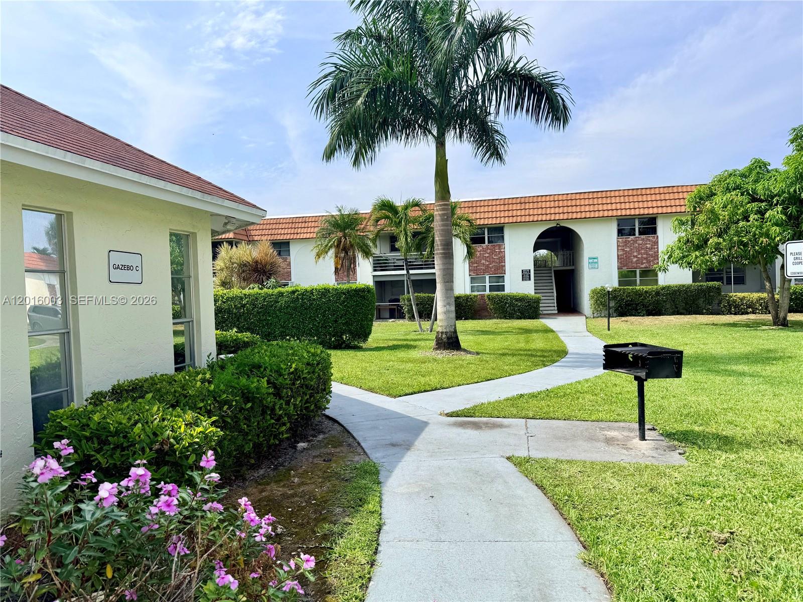 A paved walkway leads through a grassy courtyard toward a two-story apartment building — 22805 SW 66th Ave # 208, Boca Raton FL 33428, BOCA RATON, FL