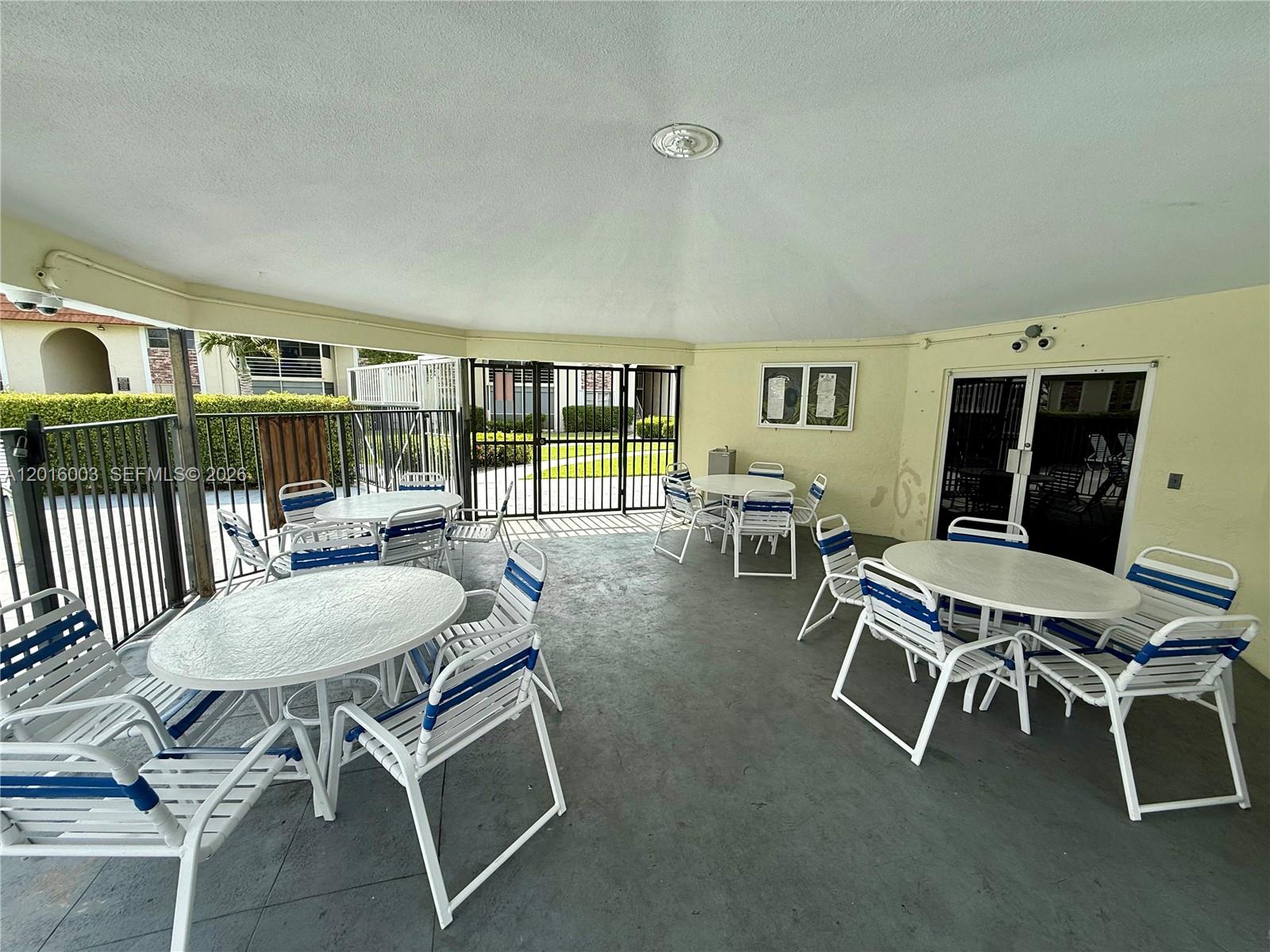 A covered outdoor patio features several round white tables with matching blue and white chairs — 22805 SW 66th Ave # 208, Boca Raton FL 33428, BOCA RATON, FL