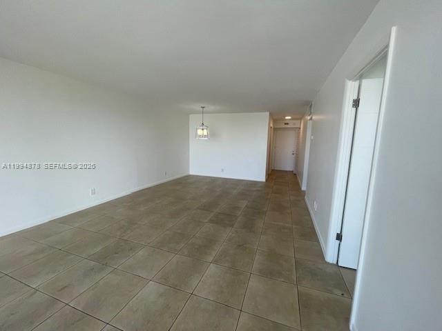 An empty room features light-colored walls, a tiled floor, and a hanging light fixture — 1830 Dixieanna St # 606, Hollywood FL 33020, HOLLYWOOD, FL