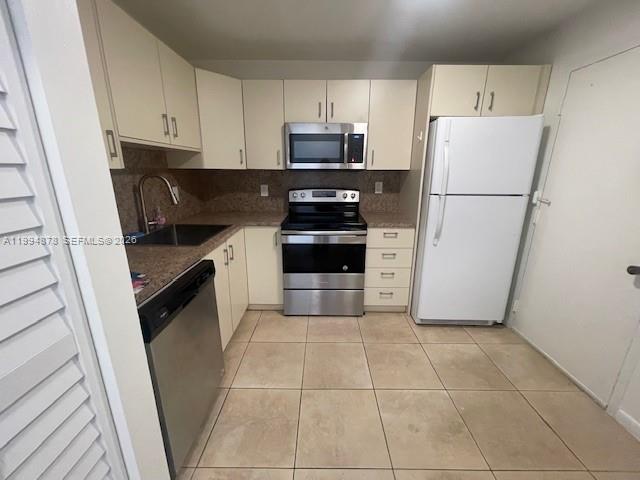 A kitchen features light-colored cabinets, stainless steel appliances, and beige tile flooring — 1830 Dixieanna St # 606, Hollywood FL 33020, HOLLYWOOD, FL