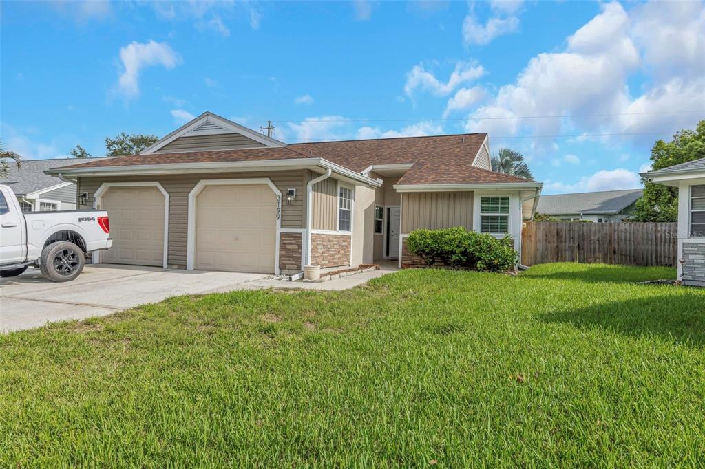 A single-story house with a two-car garage, tan siding, and a brown shingled roof — 3199 PHLOX DRIVE UNIT 214, PALM HARBOR, FL
