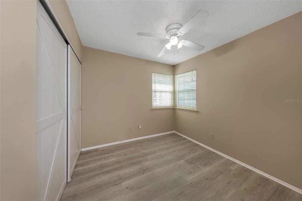 An empty bedroom features light-colored wood-look flooring, beige walls, a ceiling fan, and sliding closet doors — 3199 PHLOX DRIVE UNIT 214, PALM HARBOR, FL