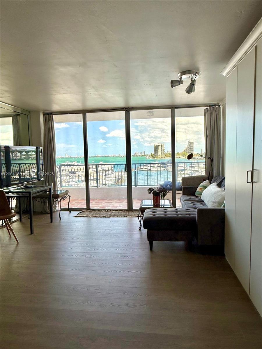 A living room with wood-look flooring, a gray sectional sofa, and floor-to-ceiling windows overlooking water — 555 NE 15th St # 420, Miami FL 33132, MIAMI, FL