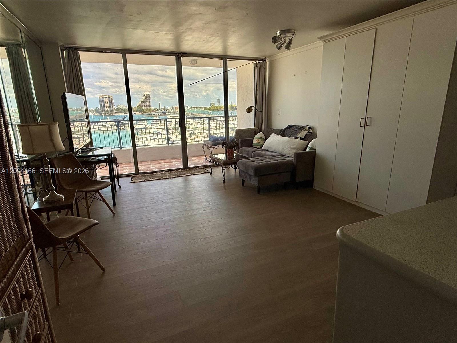 A living room with wood-look flooring, a gray sectional sofa, and a balcony overlooking water — 555 NE 15th St # 420, Miami FL 33132, MIAMI, FL