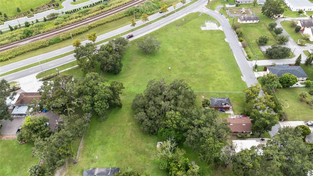 An aerial view shows a large, grassy vacant lot surrounded by trees, roads, and houses — KATHLEEN ROAD, LAKELAND, FL
